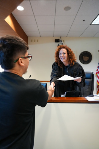 Judge Hartley shakes hands with a youth from the bench with a smile as she hands paperwork to the youth.