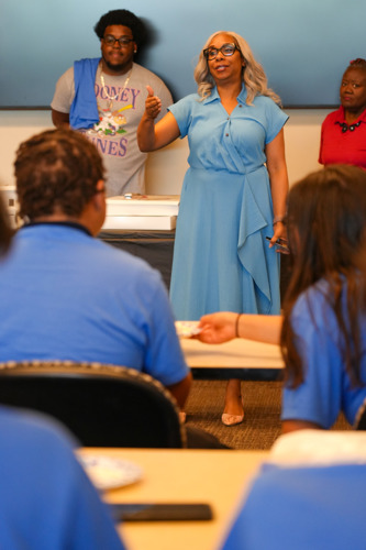 Commissioner Dyer standing in front of a group of students with two others looking on as she speaks to the group.